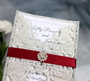 Dettaglio macro dell'invito glitterato argento tagliato al laser con nastro rosso e strass