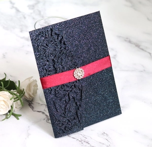 Navy blue laser cut floral wedding invitation with glitter finish and red ribbon buckle