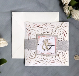Detailed view of white laser-cut wedding invitation with silver glitter belly band