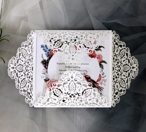 Close-up of laser-cut wedding invitation with intricate lace floral border and bird motifs