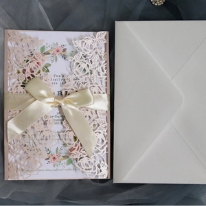 Pink laser cut rose wedding invitations with a cream satin bow and white envelopes