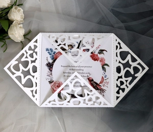 Detailed laser-cut wedding invitation featuring intricate white lace patterns and floral inserts
