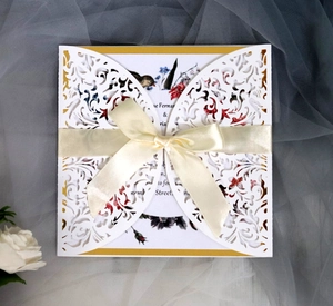 Macro view of laser-cut invitation card with gold floral inserts and satin bow