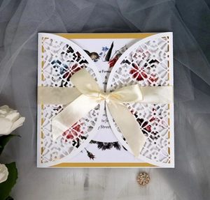 Close-up of laser-cut white lace invitation with cream ribbon bow and floral insert