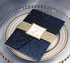 Detail of laser-cut navy blue glitter wedding invitation with golden belly band and ribbon