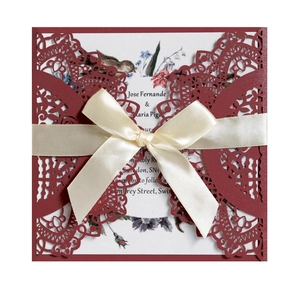Detail of burgundy laser-cut lace wedding invitation with ribbon and floral insert