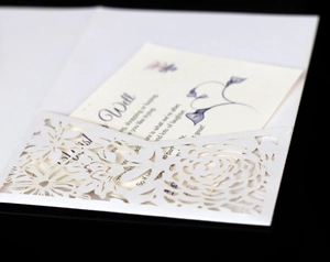Close-up of laser-cut white floral lace wedding invitation with elegant rose pattern