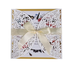 Detail of laser-cut wedding invitation with floral inner card and white satin ribbon bow