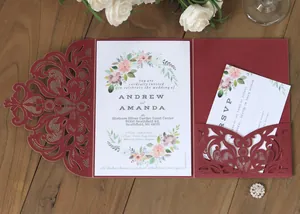 Close-up of laser-cut burgundy invitation suite with elegant floral patterns on wood background