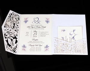 Detail of white laser-cut floral wedding invitation shell and inner cards on black background