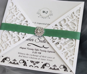 Detail einer lasergeschnittenen Hochzeitseinladung mit grünem Satinband und Brosche