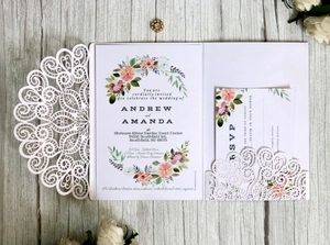 Elegant white laser-cut floral wedding invitation set with RSVP card on wood background
