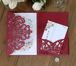 Detail of burgundy laser-cut wedding invitation with white floral card on wood