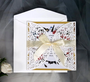 Elegant white laser-cut wedding invitation with gold lining and cream ribbon bow