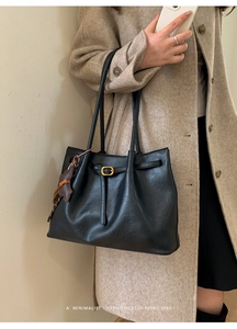 Detail of black leather shoulder bag with cat charm and gold buckle on oat coat