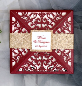 Detail of laser-cut wedding invitation sleeve with burgundy card and gold glitter band