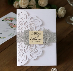 Detail of laser-cut wedding invitation with silver glitter belt and white floral pattern