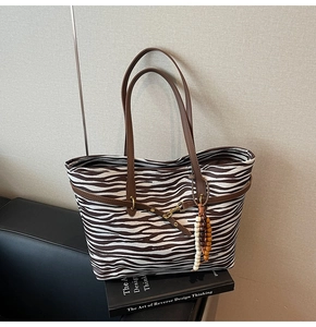 Detailed view of zebra print tote bag with brown leather handles on a black book
