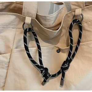 Dettaglio della borsa tote in tela beige con corda decorativa e fibbie metalliche