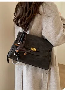 Detail of coffee brown matte shoulder bag with gold twist lock and dachshund charm on coat