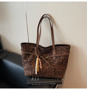 Detail of leopard print suede tote bag with brown leather handles and wooden bead charm