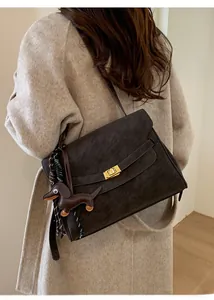 Detail of dark brown suede shoulder bag with gold clasp and dog charm on white coat