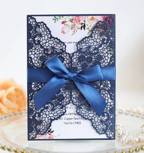 Detail of laser-cut invitation with navy blue satin bow on a decorative gold-rimmed plate