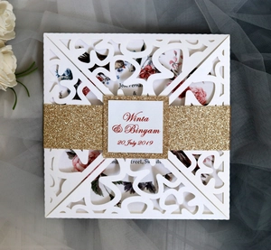 Detail of laser cut white wedding invitation with gold glitter band and floral inner page