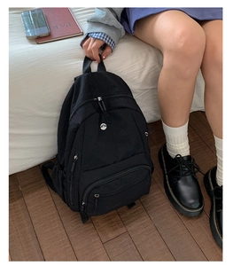 Detailaufnahme des schwarzen Nylon-Rucksacks mit M-Metalllogo und Reißverschlussfächern
