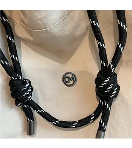 Dettaglio di un cordoncino intrecciato con punte in metallo e logo CM su borsa