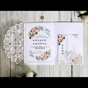 White laser cut wedding invitation with floral insert and RSVP card on wood background