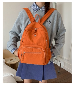 Detailansicht eines orangefarbenen Nylon-Rucksacks mit Multi-Pocket-Struktur am Modell