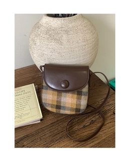 Close-up of vintage plaid saddle bag with brown leather flap and round buckle detail