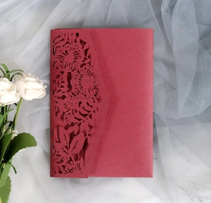 Detail of dark red laser-cut invitation cover with elegant floral lace and textured paper