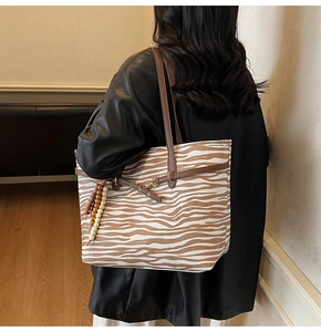 Detail shot of a zebra-print suede tote bag with brown leather straps and beaded charm