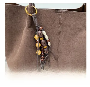 Close-up of bohemian wood bead bag charm with gold metal clasp on brown suede tote