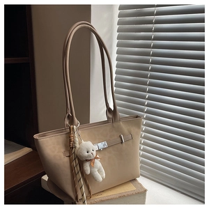 Close-up of beige tote bag with matte leather texture, metal buckle, and plush bear charm