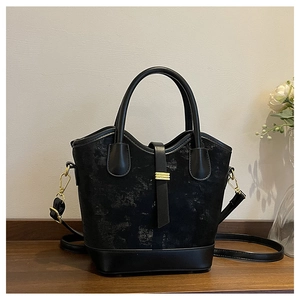 Détail du sac seau noir avec garniture dorée posé sur une surface en bois sombre