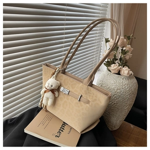 Detail of leopard print tote bag with plush bear charm and metallic lock on white background