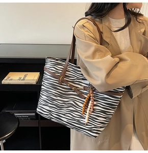 Detail of zebra print tote bag with brown straps and wooden bead tassel on a model