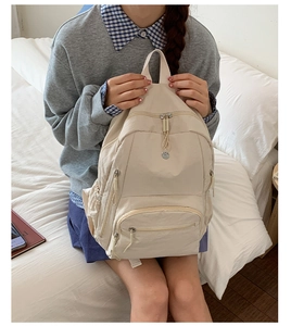 Nahaufnahme eines beigen Nylon-Rucksacks mit kleinem Rundlogo auf weißem Bett