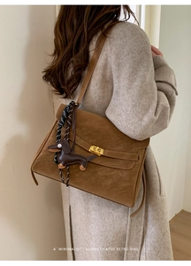 Detail of dark brown suede shoulder bag with gold clasp and dog charm on grey coat