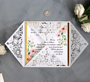 Close-up of laser-cut floral wedding invitation with gold trim card and rhinestone pin