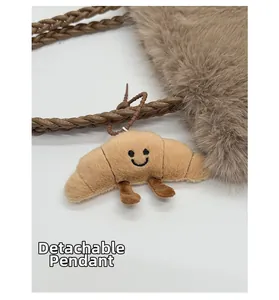 Detail of a detachable light brown plush croissant charm with embroidered smiley face