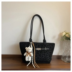 Detail of black leopard print tote bag with metal buckle and cute plush bear charm