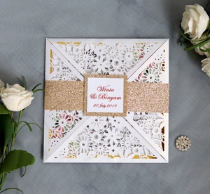 Macro shot of laser-cut floral wedding invitation with gold glitter band and white lace detail