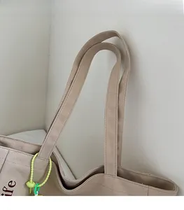 Detail of wide canvas tote straps and lime green decorative lanyard on beige bag