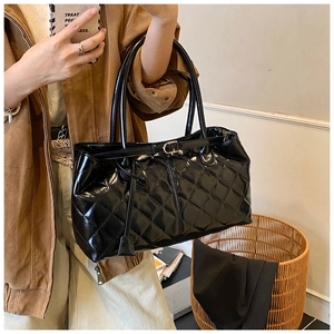 Close-up of quilted black patent leather tote bag with glossy finish and gold buckle detail