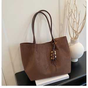 Detailed view of deep brown suede tote bag with wooden bead tassel and side stitching