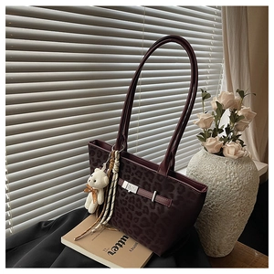 Detail of leopard print tote bag with burgundy straps, decorative buckle and bear charm